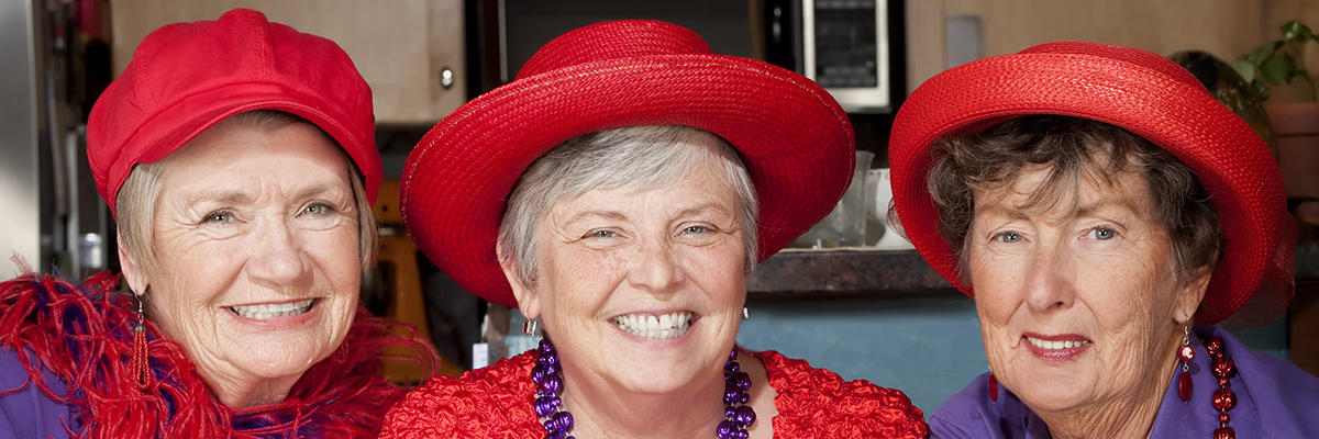 Three elderly women wearing red hats and smiling